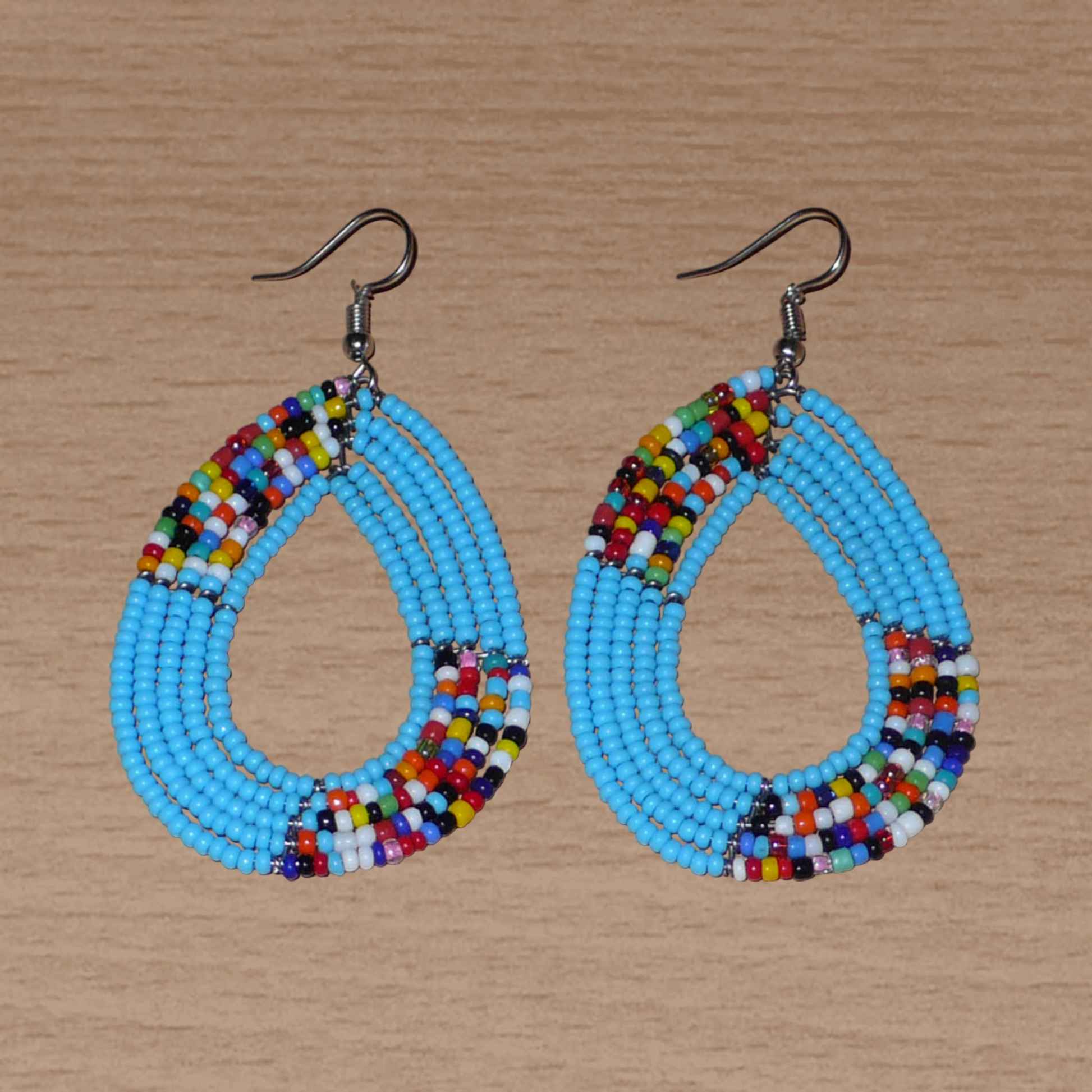 Boucles d'oreilles ethniques multi-rangs composées de perles bleu ciel et multicolores glissées sur cinq rangs de fils de fer montés en forme de gouttes. De taille moyenne, ces boucles d'oreilles kenyanes aux accents bohème mesurent 7,5 cm de long et 4 cm de large ; elles se portent avec des crochets en acier inoxydable.