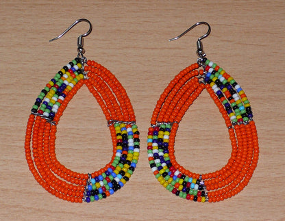 Boucles d'oreilles hippies en perles de rocaille orange et multicolores enfilées sur cinq rangées de fils de fer montés en forme de gouttes. Elles mesurent 8 cm de long et 4,5 cm de large et se portent sur des oreilles percées.