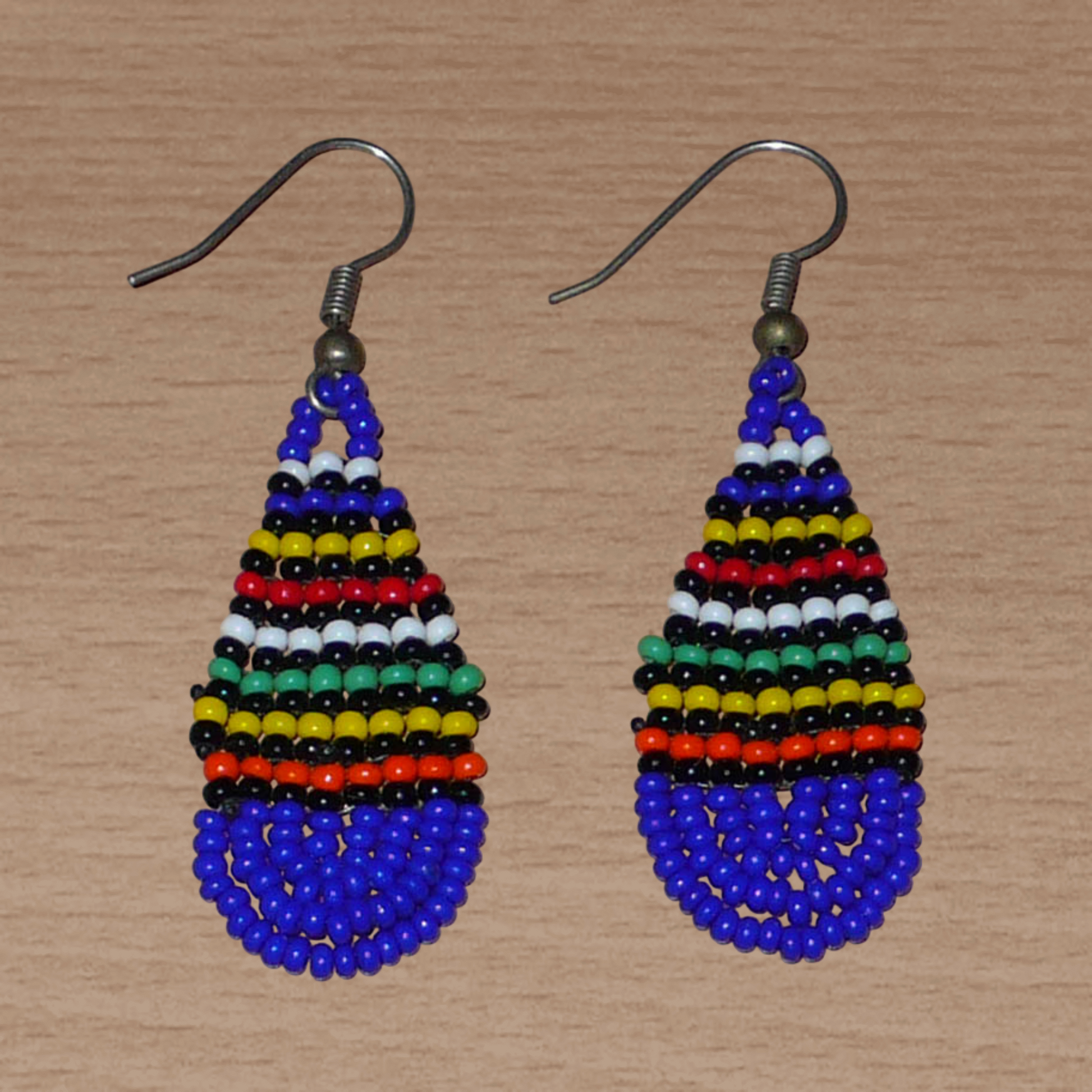 Petites boucles d'oreilles sud-africaines de tradition ethnique zouloue composée d'un tissage de perles de rocaille bleu foncé et multicolores. Cette paire de boucles d'oreilles traditionnelles mesure 5.5 cm de long et 2 cm de large, et se portent avec des crochets en acier inoxydable sur des oreilles percées.