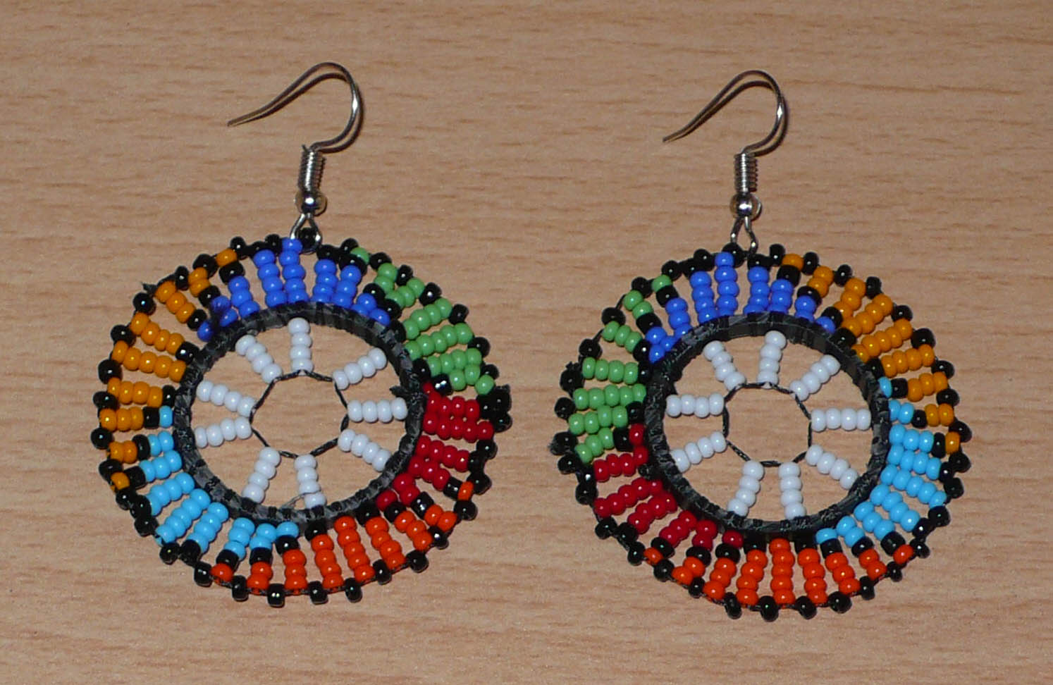 Boucles d'oreilles ethniques rondes à motifs sud-africains zoulous composées de perles de rocaille blanches et multicolores. De taille moyenne et légères à porter, elles mesurent 6 cm de long et 4 cm de large, et se portent sur des oreilles percées.