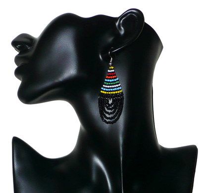 Boucles d'oreilles ethniques de tradition sud-africaine en forme de gouttes composées d'un tissage de perles de rocaille noires et multicolores. Elles mesurent 7 cm de long et 2,5 cm de large et se portent sur des oreilles percées. Présentées sur un mannequin. Timeless Fineries
