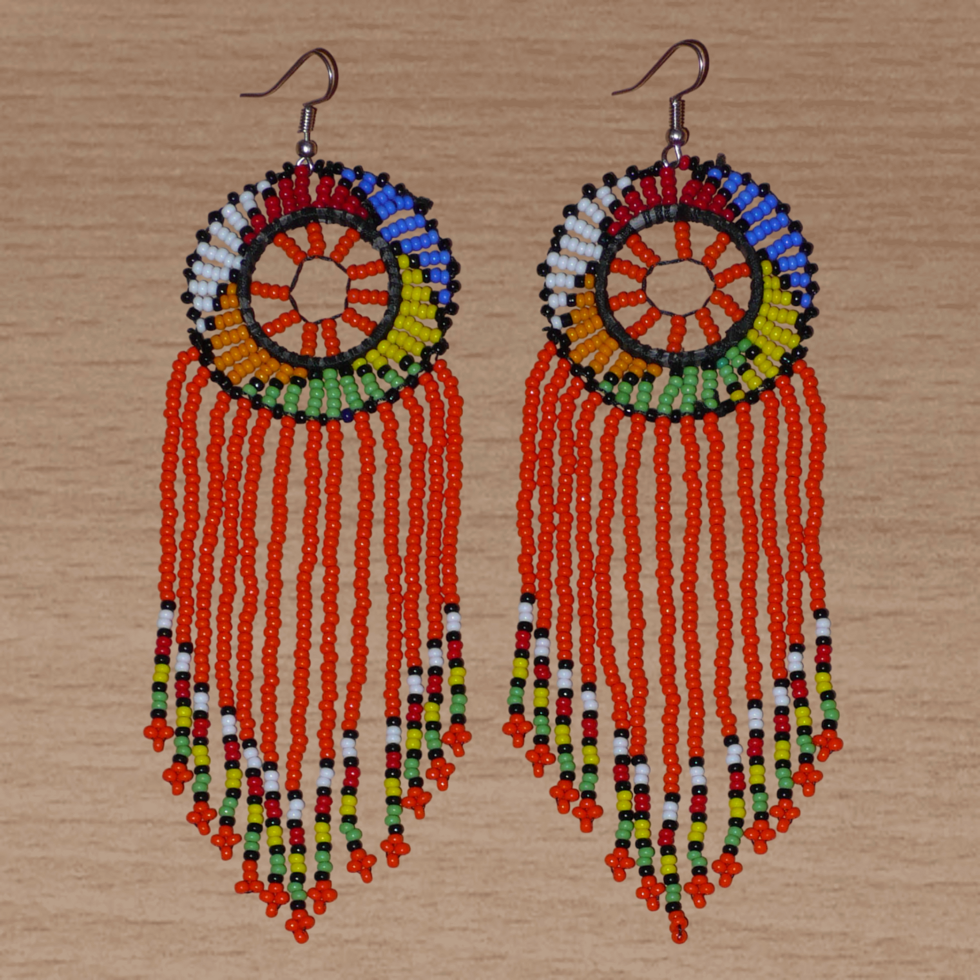 Longues boucles d'oreilles sud-africaines à franges et motifs traditionnels zoulous composées de perles de rocaille orange et multicolores. Elles mesurent 14,5 cm de long et 4,5 cm de large.