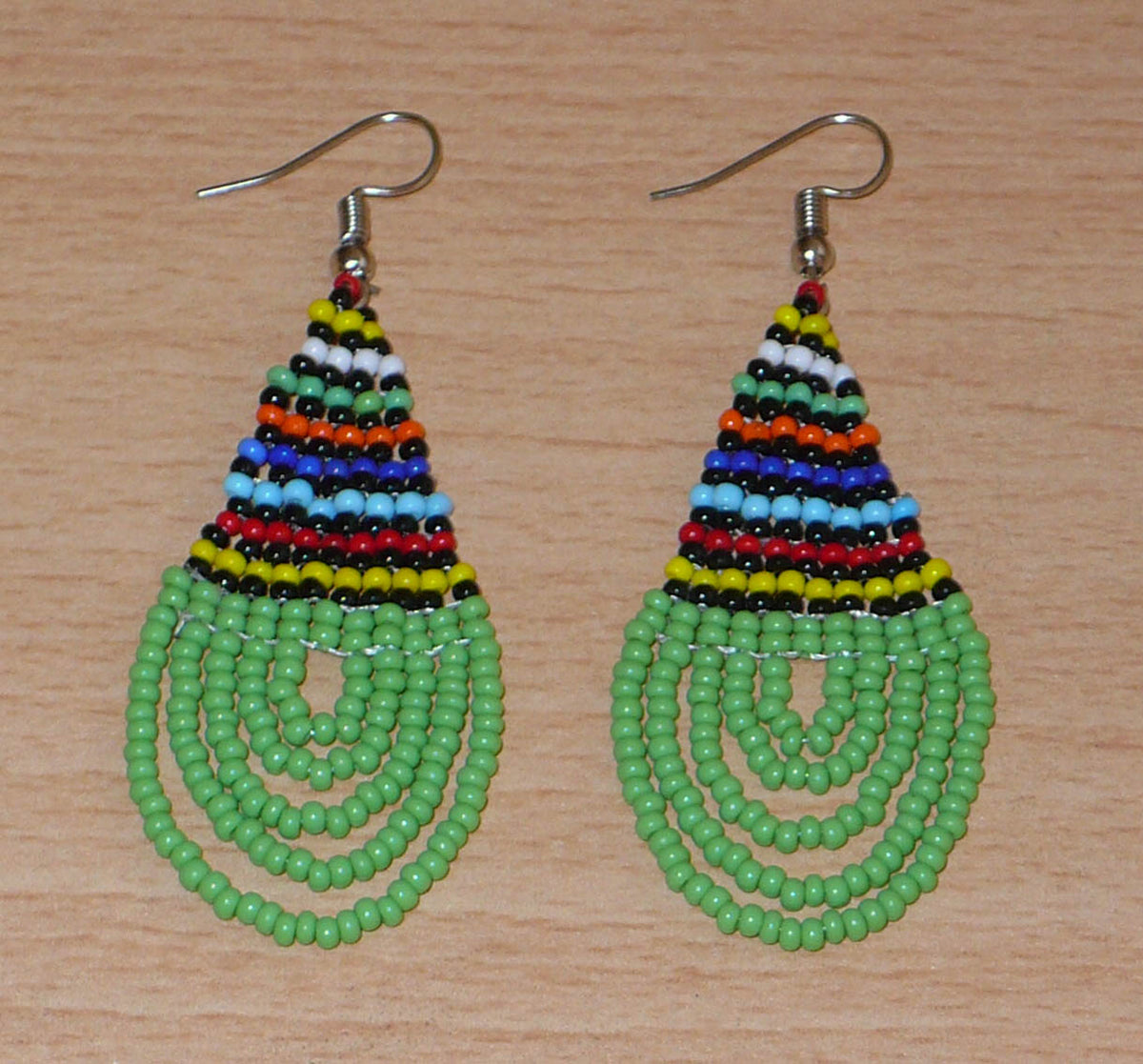 Boucles d'oreilles africaines traditionnelles zouloues en forme de gouttes faites d'un tissage de perles de rocaille vertes et multicolores. Elles mesurent 7 cm de long et 2,5 cm de large et se portent sur des oreilles percées.