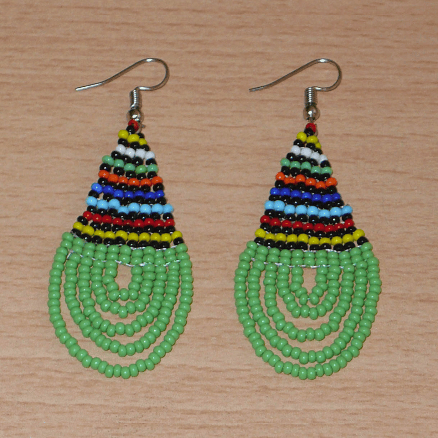 Boucles d'oreilles africaines traditionnelles zouloues en forme de gouttes faites d'un tissage de perles de rocaille vertes et multicolores. Elles mesurent 7 cm de long et 2,5 cm de large et se portent sur des oreilles percées. 