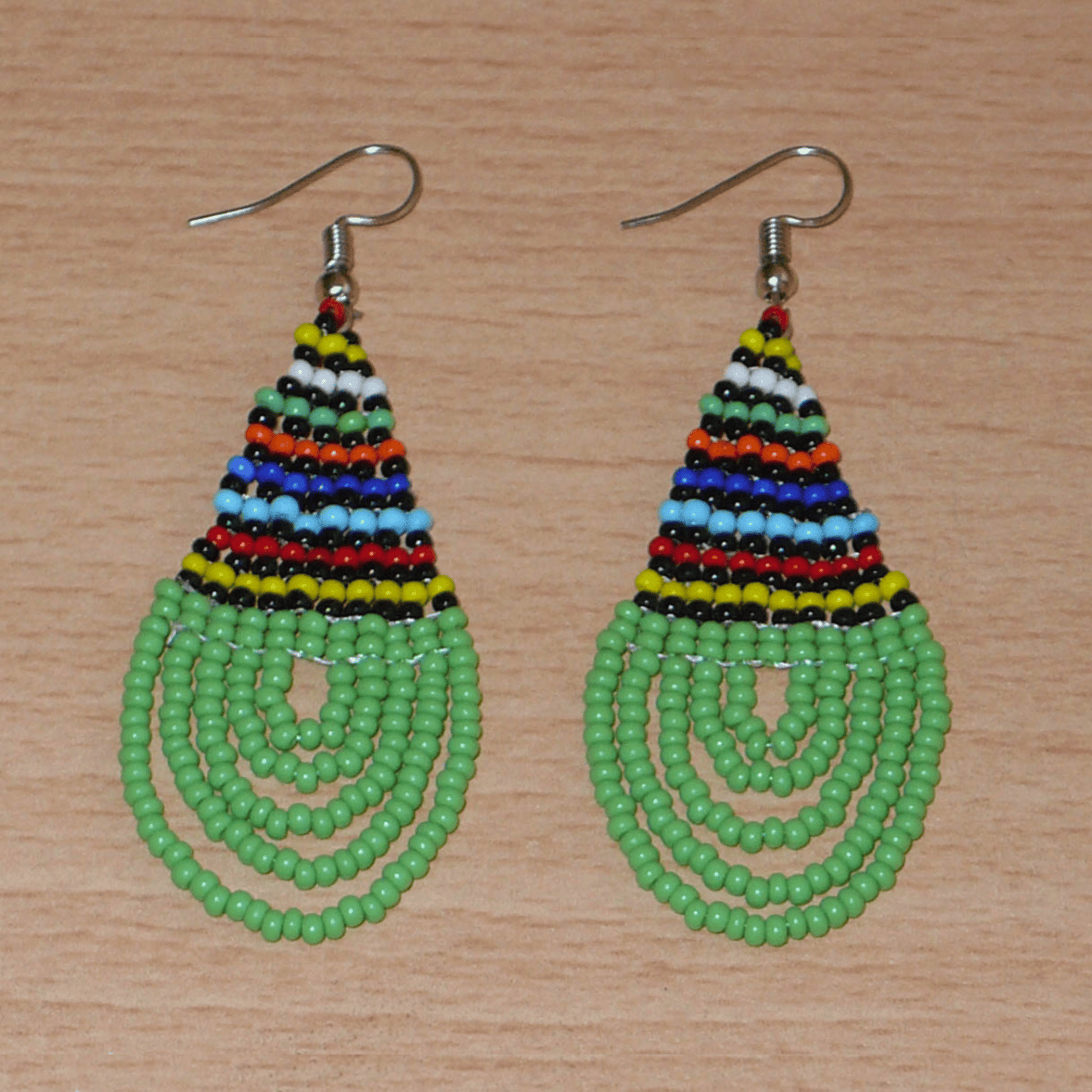 Boucles d'oreilles africaines traditionnelles zouloues en forme de gouttes faites d'un tissage de perles de rocaille vertes et multicolores. Elles mesurent 7 cm de long et 2,5 cm de large et se portent sur des oreilles percées. 