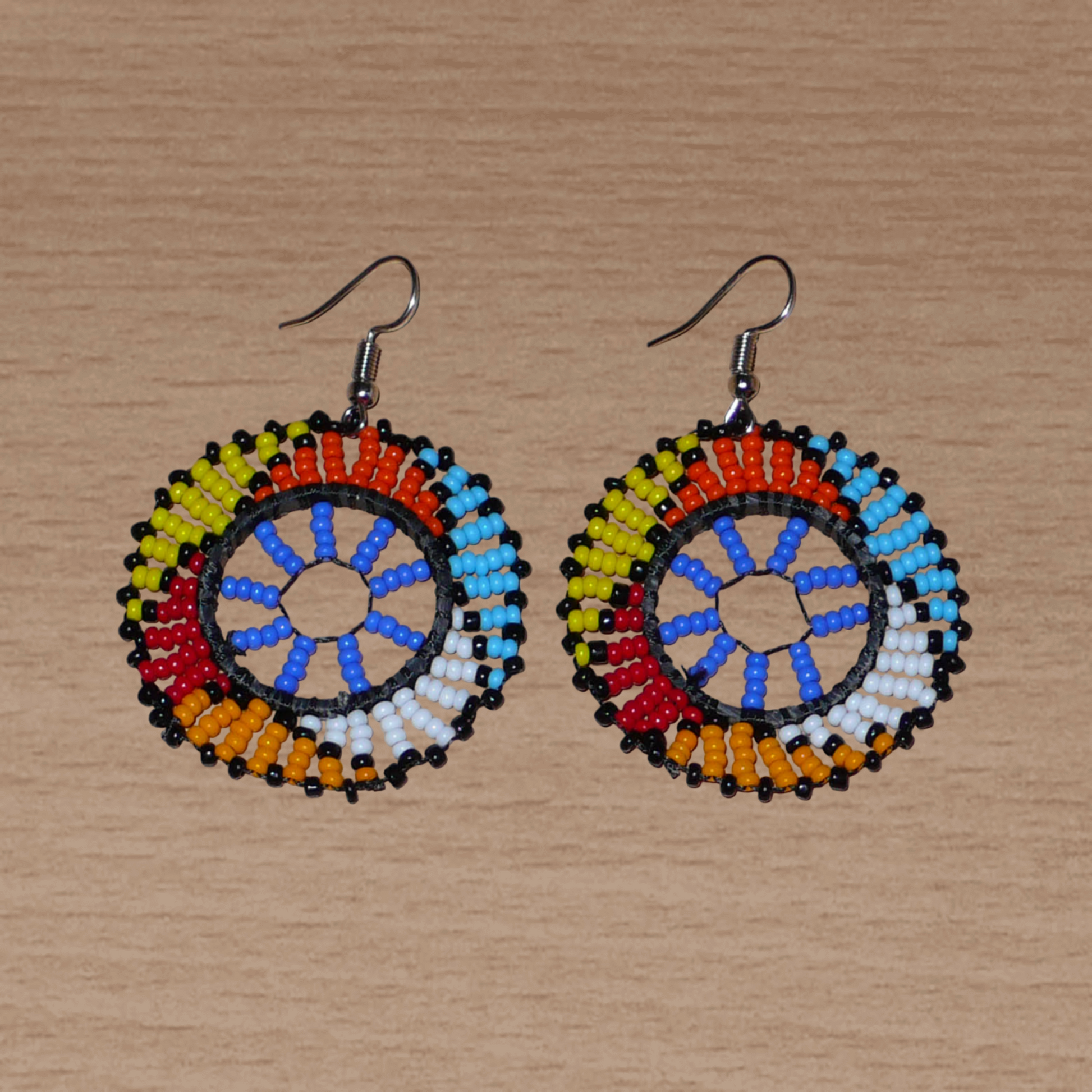 Boucles d'oreilles africaines rondes à motifs ethniques zoulous composées de perles de rocaille bleues et multicolores. De taille moyenne et légères à porter, elles mesurent 6 cm de long et 4 cm de large. Elles se portent avec des crochets en acier inoxydable sur des oreilles percées.