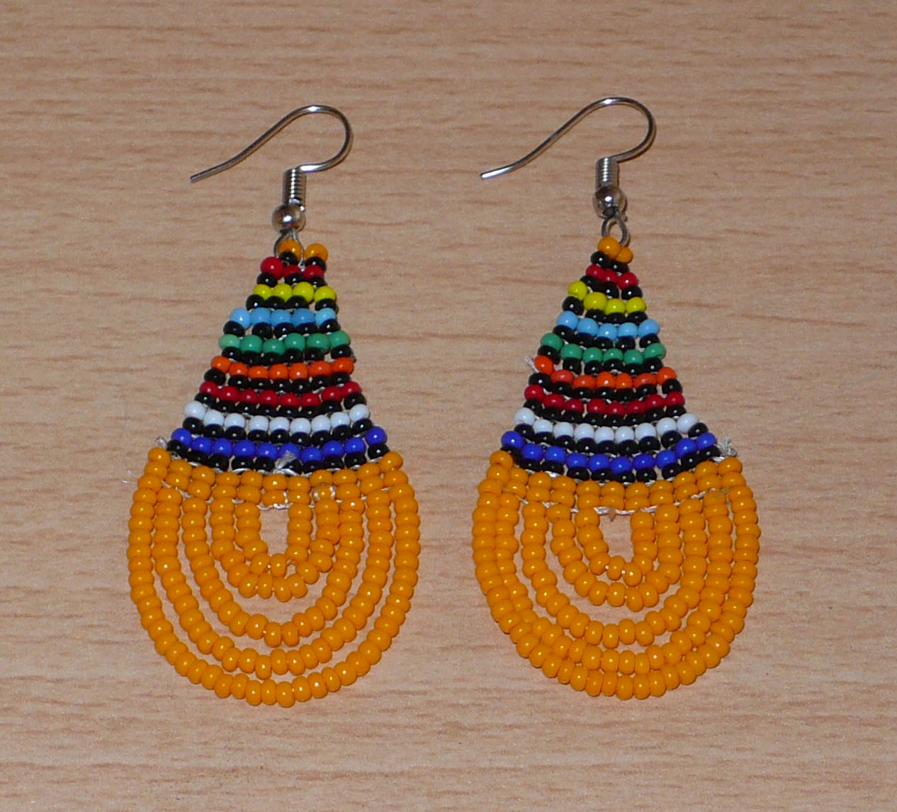 Boucles d'oreilles africaines traditionnelles en forme de gouttes composées d'un tissage de perles de rocaille orange et multicolores. Elles mesurent 7 cm de long et 2,5 cm de large. 