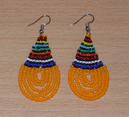 Boucles d'oreilles africaines traditionnelles en forme de gouttes composées d'un tissage de perles de rocaille orange et multicolores. Elles mesurent 7 cm de long et 2,5 cm de large. 