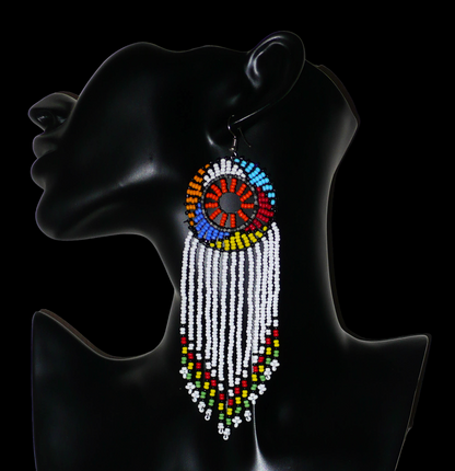 Longues boucles d'oreilles sud-africaines à franges et motifs traditionnels zoulous composées de perles de rocaille blanches, orange et multicolores. Elles mesurent 14,5 cm de long et 4,5 cm de large, et se portent avec des crochets en acier inoxydable sur des oreilles percées.