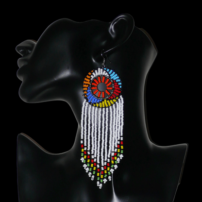 Longues boucles d'oreilles sud-africaines à franges et motifs traditionnels zoulous composées de perles de rocaille blanches, orange et multicolores. Elles mesurent 14,5 cm de long et 4,5 cm de large, et se portent avec des crochets en acier inoxydable sur des oreilles percées.