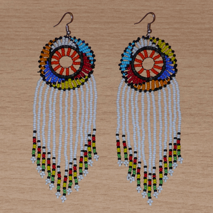 Longues boucles d'oreilles sud-africaines à franges et motifs traditionnels zoulous composées de perles de rocaille blanches, orange et multicolores. Elles mesurent 14,5 cm de long et 4,5 cm de large, et se portent avec des crochets en acier inoxydable sur des oreilles percées.