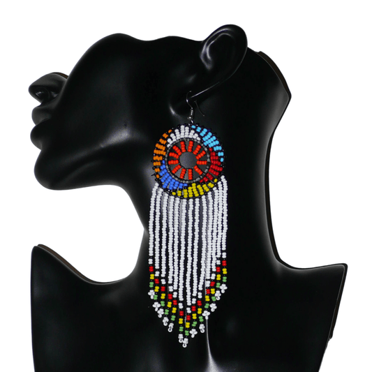 Longues boucles d'oreilles sud-africaines à franges et motifs traditionnels zoulous composées de perles de rocaille blanches, orange et multicolores. Elles mesurent 14,5 cm de long et 4,5 cm de large, et se portent avec des crochets en acier inoxydable sur des oreilles percées.