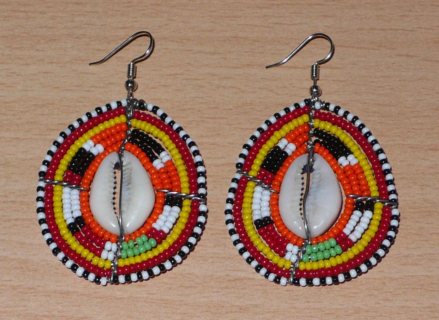 Boucles d'oreilles africaines en forme de boucliers Massai composées de perles et de coquillages. Elles mesurent 7 cm de long et 4 cm de large et se portent sur des oreilles percées. Timeless Fineries
