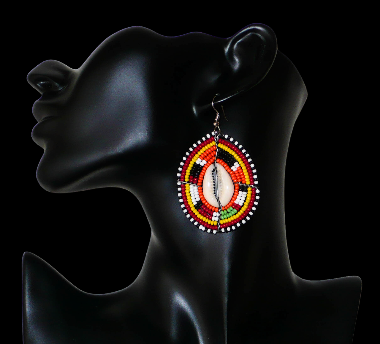 Boucles d'oreilles africaines en forme de boucliers Massai composées de perles et de coquillages. Elles mesurent 7 cm de long et 4 cm de large et se portent sur des oreilles percées.