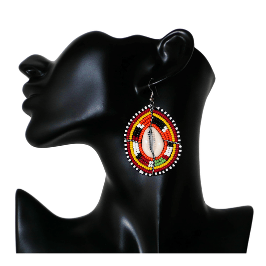 Boucles d'oreilles africaines en forme de boucliers Massai composées de perles et de coquillages. Elles mesurent 7 cm de long et 4 cm de large et se portent sur des oreilles percées.