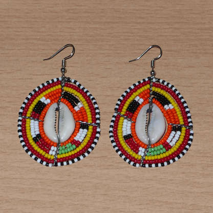 Boucles d'oreilles africaines en forme de boucliers Massai composées de perles et de coquillages. Elles mesurent 7 cm de long et 4 cm de large et se portent sur des oreilles percées.