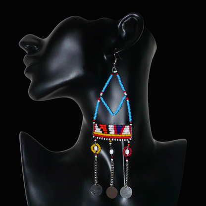 Longues boucles d'oreilles africaines Massai bleues et multicolores composées de perles de rocaille bleues et multicolores et de perles en plastique blanc glissées sur des structures géométriques en fils de fer ; elles se prolongent de chaînettes décorées de disques métalliques. Surdimensionnées, elles mesurent 15.5 cm de long et se portent sur des oreilles percées.