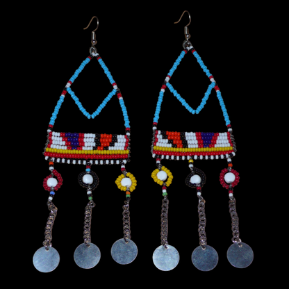 Longues boucles d'oreilles africaines Massai bleues et multicolores composées de perles de rocaille bleues et multicolores et de perles en plastique blanc glissées sur des structures géométriques en fils de fer ; elles se prolongent de chaînettes décorées de disques métalliques. Surdimensionnées, elles mesurent 15.5 cm de long et se portent sur des oreilles percées.