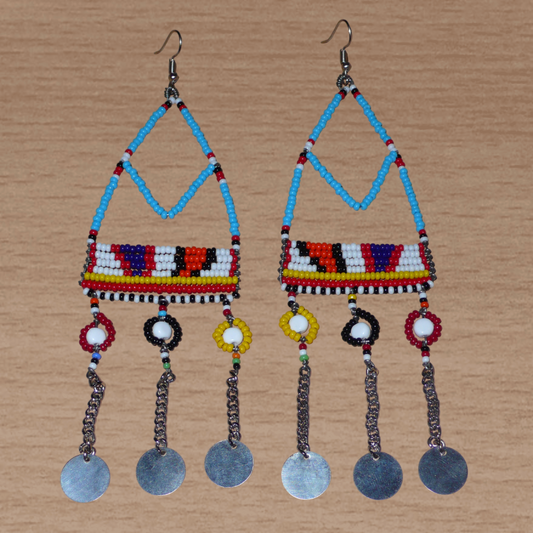 Longues boucles d'oreilles africaines Massai bleues et multicolores composées de perles de rocaille bleues et multicolores et de perles en plastique blanc glissées sur des structures géométriques en fils de fer ; elles se prolongent de chaînettes décorées de disques métalliques. Surdimensionnées, elles mesurent 15.5 cm de long et se portent sur des oreilles percées.