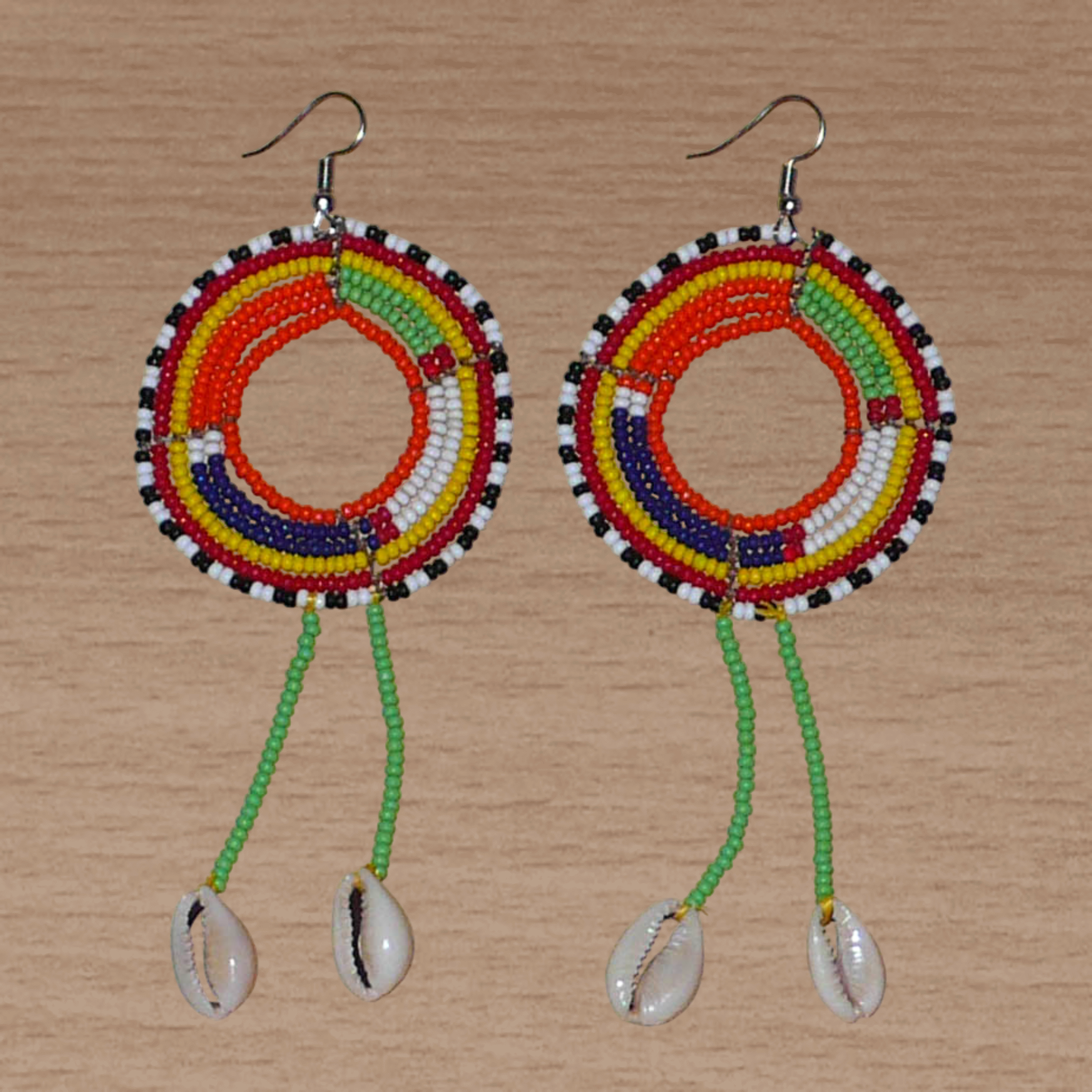 Longues boucles d'oreilles africaines tribales Massai composées de perles de rocaille vertes et multicolores glissées sur une structure ronde en fils de fer et prolongées de franges perlées ornées de coquillages. Elles mesurent 12.5 cm de long et 5 cm de large et se portent sur des oreilles percées.