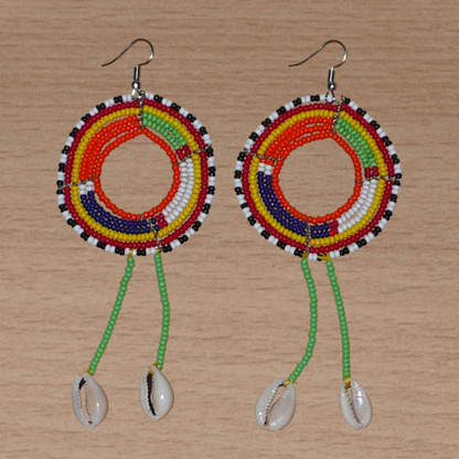 Longues boucles d'oreilles africaines tribales Massai composées de perles de rocaille vertes et multicolores glissées sur une structure ronde en fils de fer et prolongées de franges perlées ornées de coquillages. Elles mesurent 12.5 cm de long et 5 cm de large et se portent sur des oreilles percées.