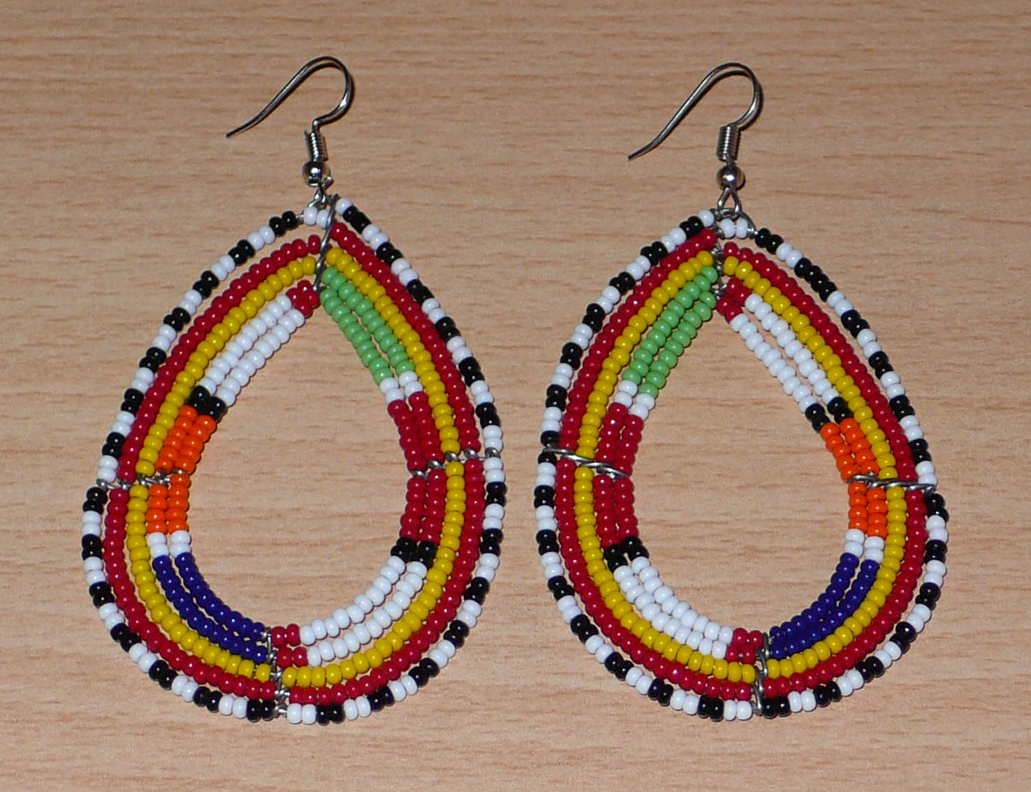 Boucles d'oreilles africaines de tradition tribale Massai composées de perles de rocaille multicolores glissées sur cinq rangées de fils de fer montés en forme de gouttes. Elles mesurent 8.3 cm de long et 4.5 cm de large, et se portent sur des oreilles percées.