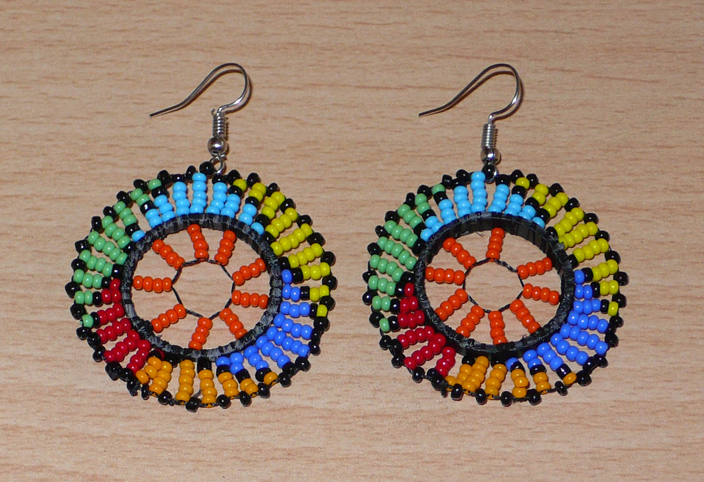 Boucles d'oreilles africaines rondes à motifs ethniques zoulous composées de perles de rocaille orange et multicolores glissées sur des fils de nylon fixés sur des structures circulaires en plastique. Elles mesurent 6 cm de long et 4 cm de large et se portent sur des oreilles percées. Timeless Fineries