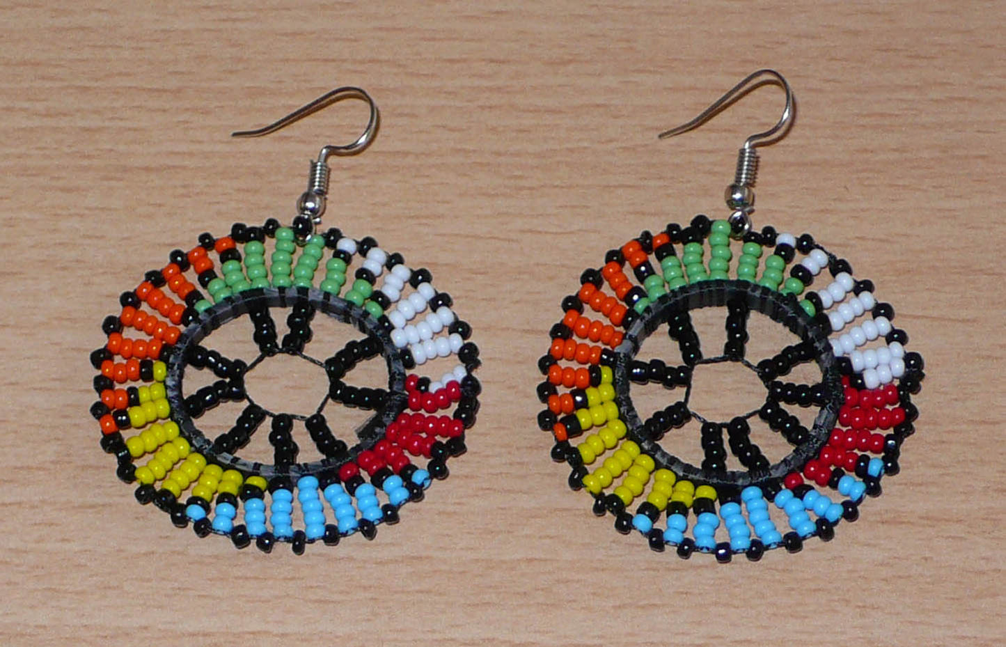 Boucles d'oreilles ethniques rondes à motifs zoulous composées de perles de rocaille noires et multicolores. De taille moyenne et légères à porter, elles mesurent 6 cm de long et 4 cm de large. 