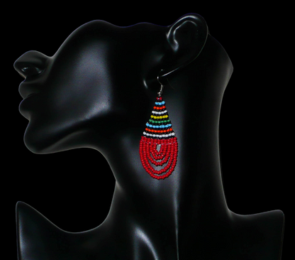 Bijoux africains rouges. Boucles d'oreilles sud-africaines en forme de gouttes faites d'un tissage de perles de rocaille rouges et multicolores. Elles mesurent 7 cm de long et 2,5 cm de large et se portent sur des oreilles percées. Timeless Fineries