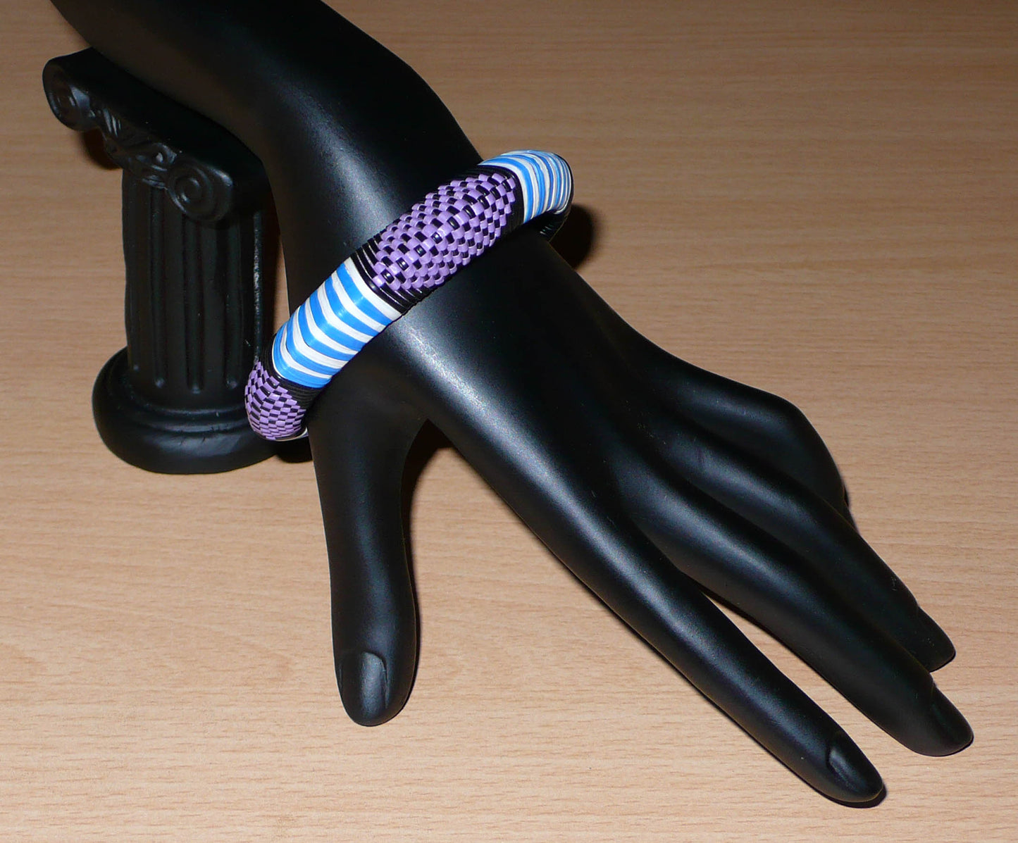 Bracelet africain à motifs ethniques rayés et à damiers composé d'un tissage de fines bandelettes de plastique recyclé violet, bleu, noir et blanc.