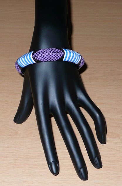 Bracelet africain à motifs ethniques rayés et à damiers composé d'un tissage de fines bandelettes de plastique recyclé violet, bleu, noir et blanc.