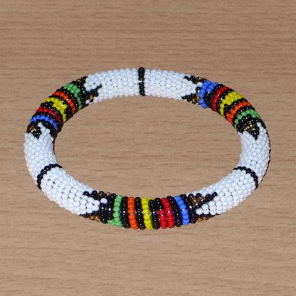 Bracelet africain tubulaire à motifs traditionnels zoulous composé de perles de rocaille blanches et multicolores ; glissées sur du fil de nylon, les perles sont ensuite enroulées autour d'un tube en plastique. Ce bracelet a une circonférence de 21 cm, un diamètre de 6.5 cm, et une épaisseur de 1 cm.