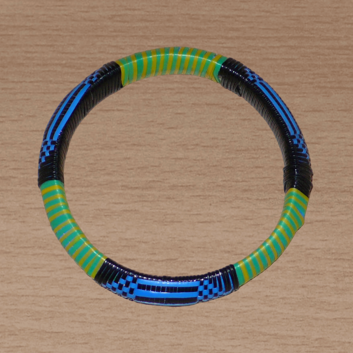 Bracelet africain malien à motifs ethniques : fabriqué dans une démarche eco-responsable, il est tressé avec de fines bandes de plastique recyclé noir, bleu, vert et jaune. La circonférence interne de ce bracelet est de 21 cm, avec un diamètre interne de 6.8 cm et une épaisseur de 1.3 cm.
