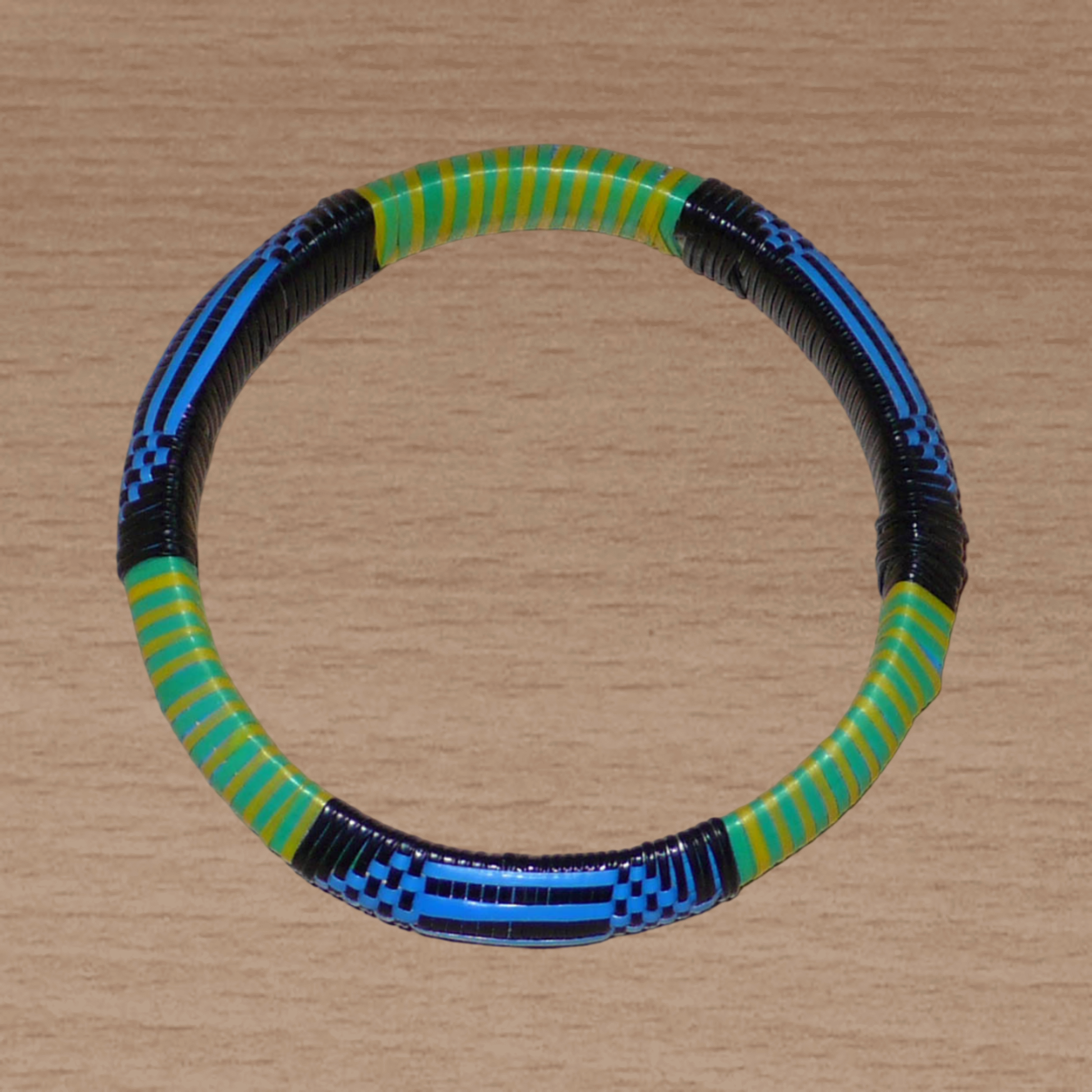 Bracelet africain malien à motifs ethniques : fabriqué dans une démarche eco-responsable, il est tressé avec de fines bandes de plastique recyclé noir, bleu, vert et jaune. La circonférence interne de ce bracelet est de 21 cm, avec un diamètre interne de 6.8 cm et une épaisseur de 1.3 cm.