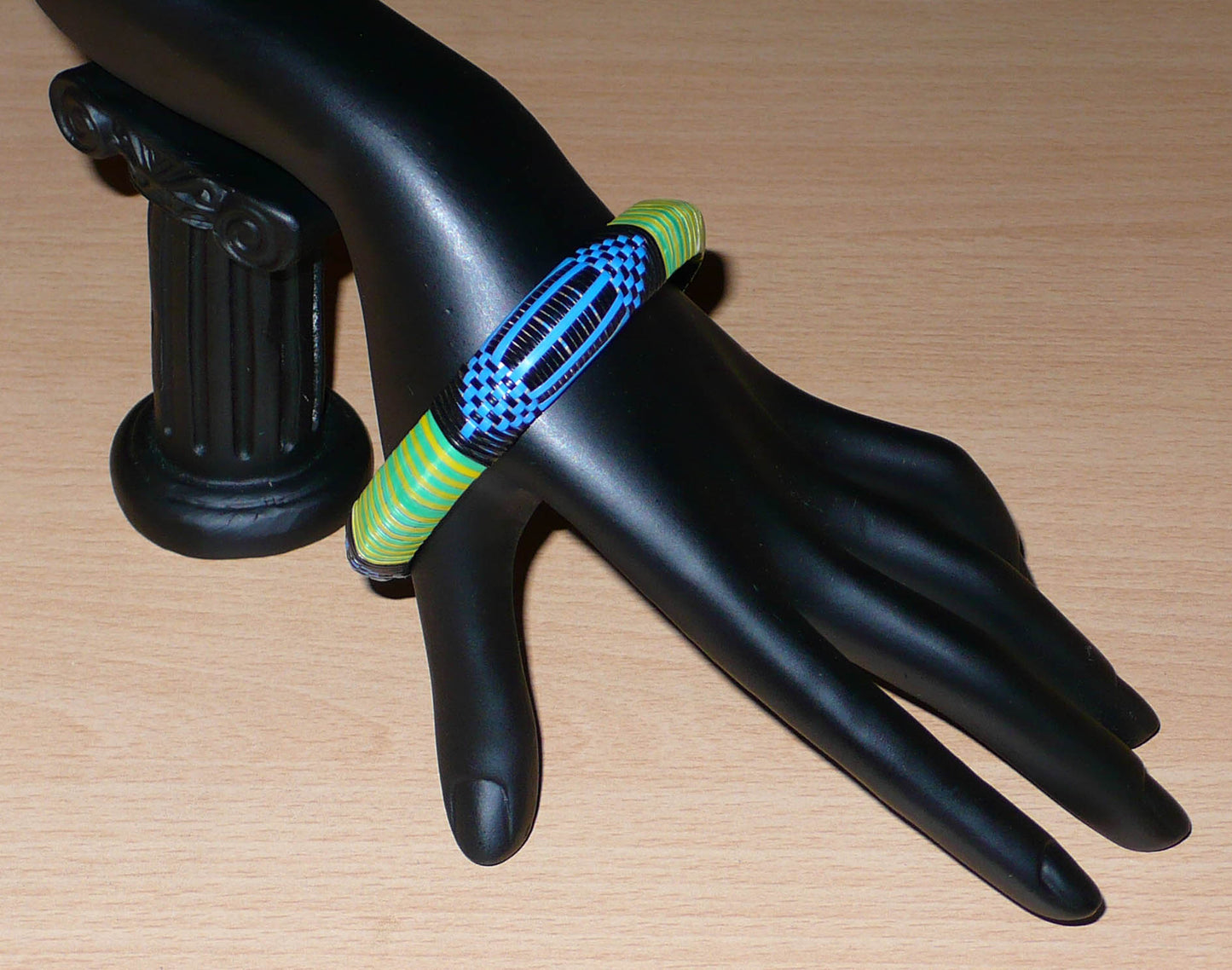 Bracelet africain malien à motifs ethniques : fabriqué dans une démarche eco-responsable, il est tressé avec de fines bandes de plastique recyclé noir, bleu, vert et jaune. La circonférence interne de ce bracelet est de 21 cm, avec un diamètre interne de 6.8 cm et une épaisseur de 1.3 cm.
