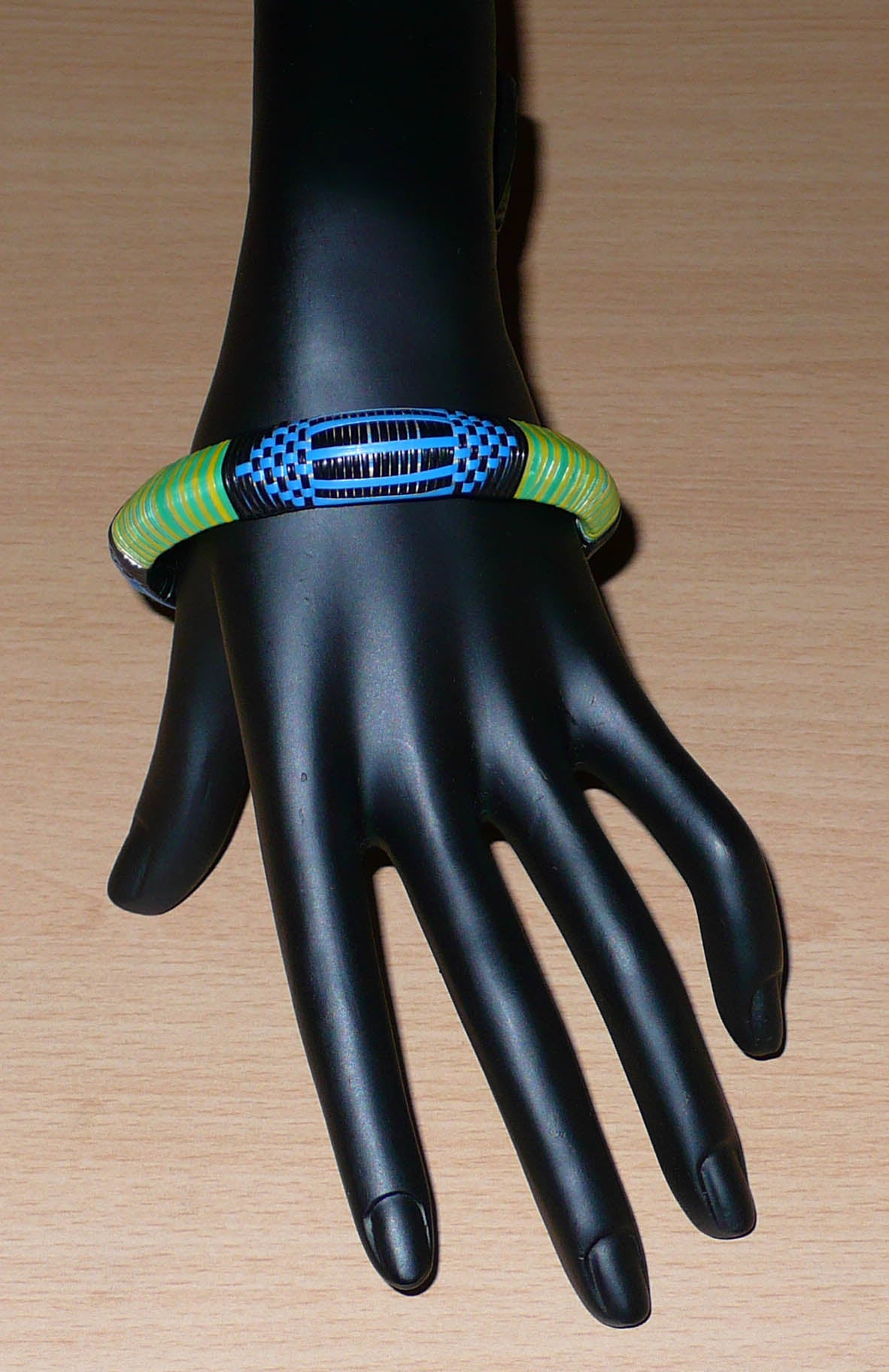 Bracelet africain malien à motifs ethniques : fabriqué dans une démarche eco-responsable, il est tressé avec de fines bandes de plastique recyclé noir, bleu, vert et jaune. La circonférence interne de ce bracelet est de 21 cm, avec un diamètre interne de 6.8 cm et une épaisseur de 1.3 cm.