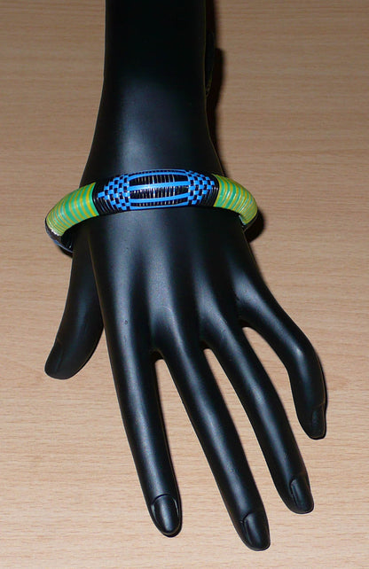 Bracelet africain malien à motifs ethniques : fabriqué dans une démarche eco-responsable, il est tressé avec de fines bandes de plastique recyclé noir, bleu, vert et jaune. La circonférence interne de ce bracelet est de 21 cm, avec un diamètre interne de 6.8 cm et une épaisseur de 1.3 cm.