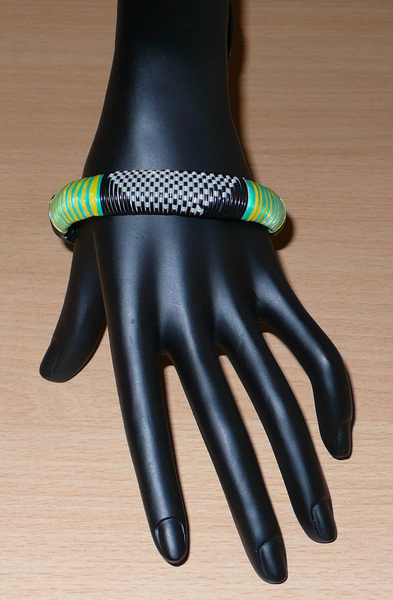 Bracelet africain eco-friendly tressé avec des fines bandes de plastique recyclé noir, blanc, vert et jaune.