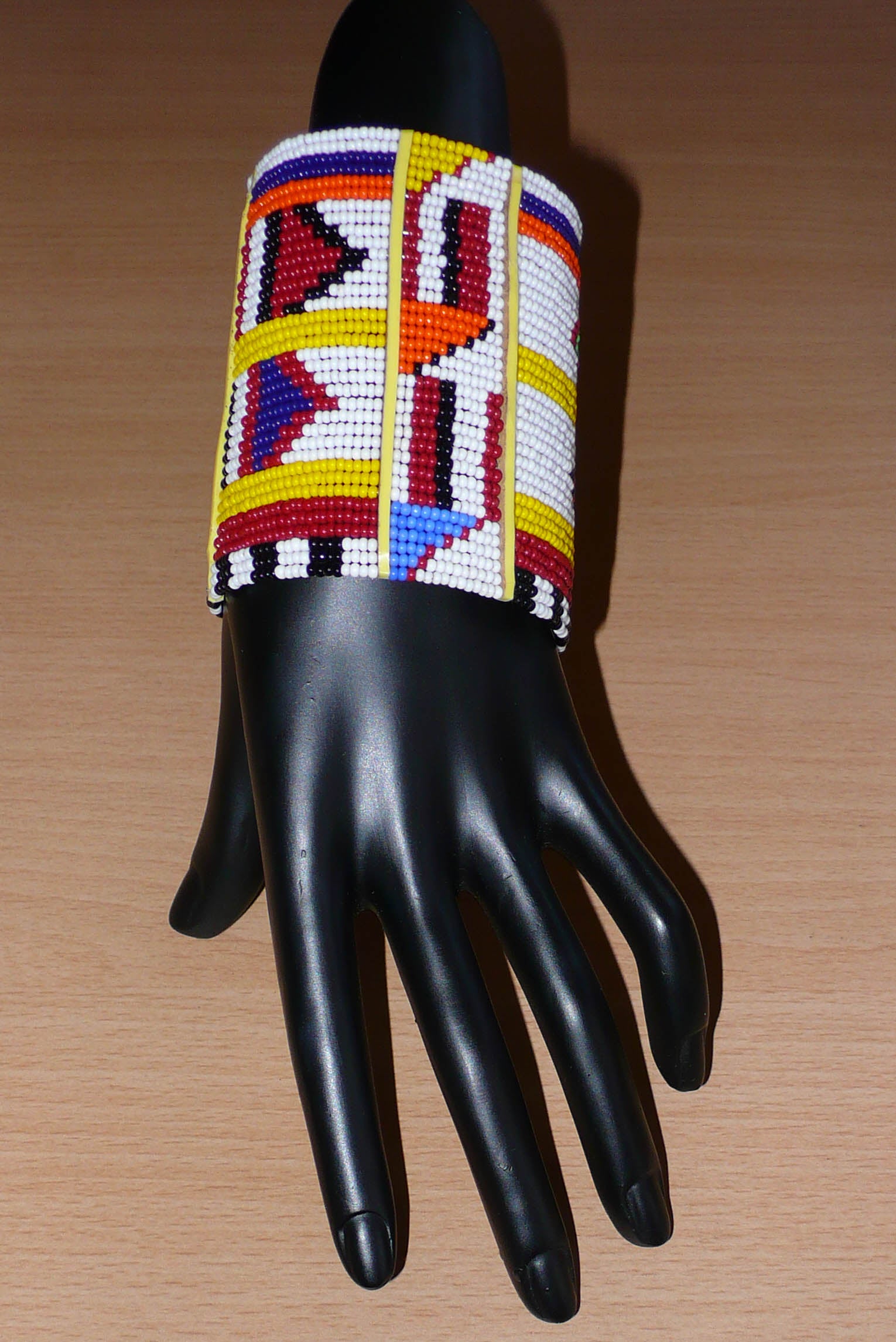 Bracelet africain Massai multi-rangs à motifs ethniques composé de trente-six rangées de perles de rocaille blanches et multicolores glissées sur des fils de fer fixés sur des charnières en plastique jaune.