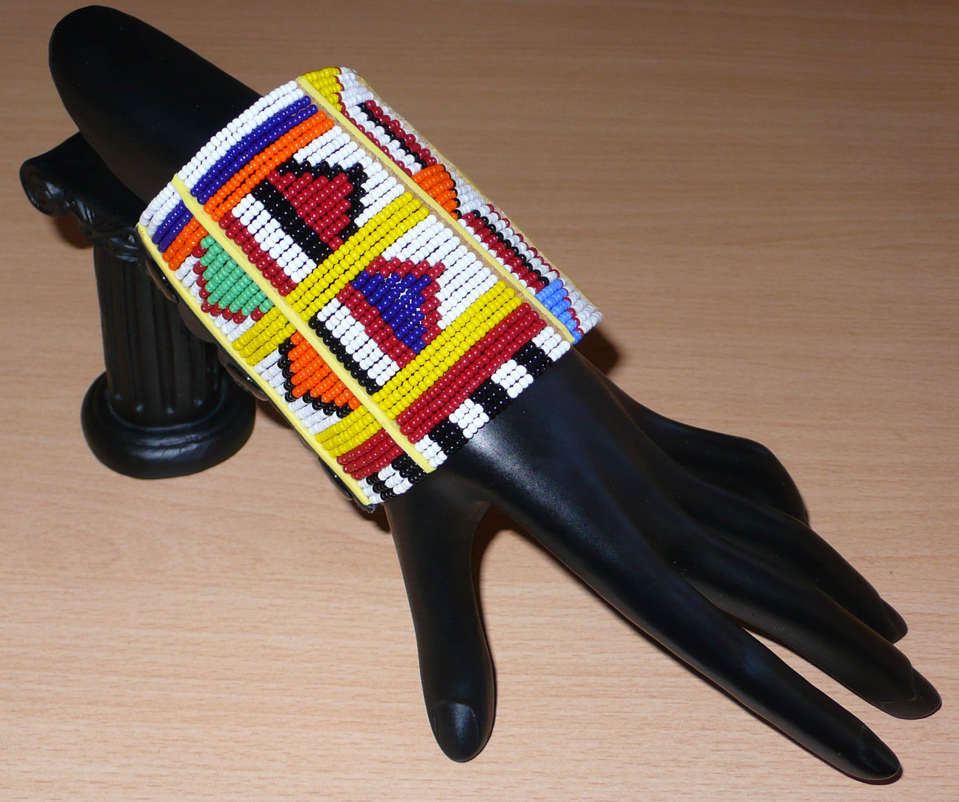 Bracelet africain Massai multi-rangs à motifs ethniques composé de trente-six rangées de perles de rocaille blanches et multicolores glissées sur des fils de fer fixés sur des charnières en plastique jaune.