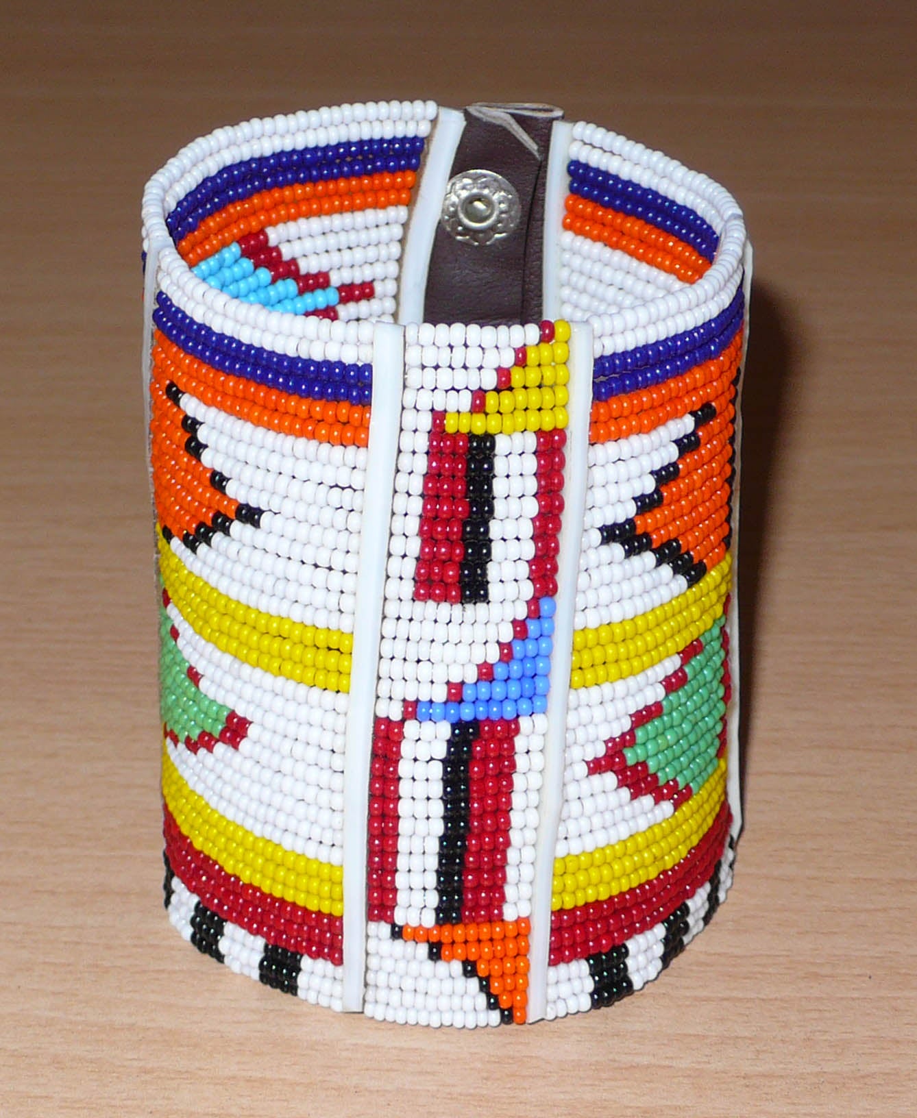 Bracelet africain traditionnel Massai aux couleurs exotiques composé de plusieurs rangées de perles de rocaille blanches et multicolores glissées sur des fils de fer fixés sur des charnières en plastique blanc.