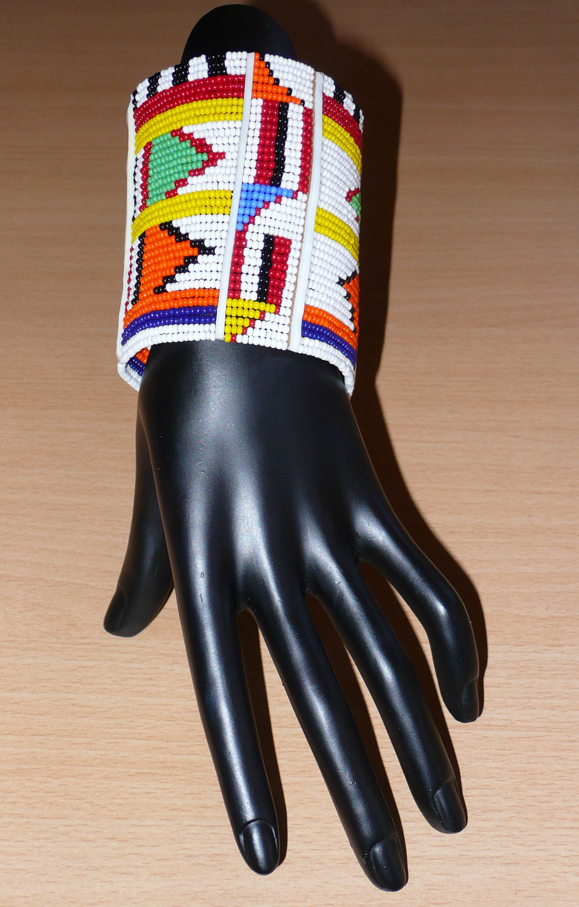 Bracelet africain traditionnel Massai aux couleurs exotiques composé de plusieurs rangées de perles de rocaille blanches et multicolores glissées sur des fils de fer fixés sur des charnières en plastique blanc.