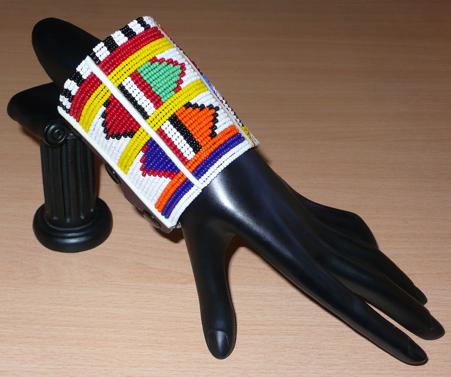 Bracelet africain traditionnel Massai aux couleurs exotiques composé de plusieurs rangées de perles de rocaille blanches et multicolores glissées sur des fils de fer fixés sur des charnières en plastique blanc.