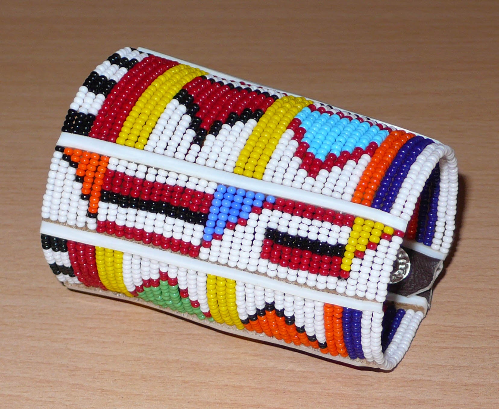 Bracelet africain pour enfant à motifs ethniques traditionnels Massai composé de trente-six rangées de perles de rocaille blanches et multicolores glissées sur des fils de fer fixés sur des charnières en plastique blanc.