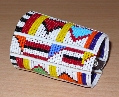 Bracelet africain pour enfant à motifs ethniques traditionnels Massai composé de trente-six rangées de perles de rocaille blanches et multicolores glissées sur des fils de fer fixés sur des charnières en plastique blanc.