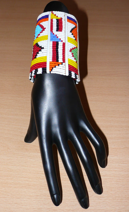 Bracelet africain pour enfant à motifs ethniques traditionnels Massai composé de trente-six rangées de perles de rocaille blanches et multicolores glissées sur des fils de fer fixés sur des charnières en plastique blanc.