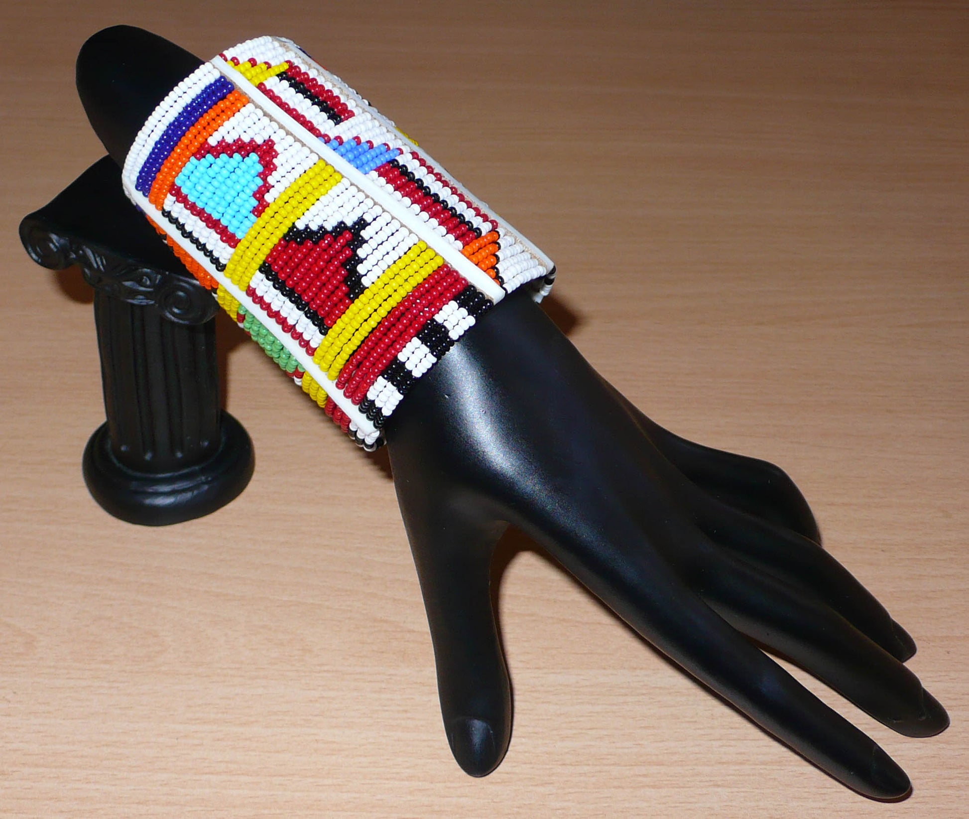 Bracelet africain pour enfant à motifs ethniques traditionnels Massai composé de trente-six rangées de perles de rocaille blanches et multicolores glissées sur des fils de fer fixés sur des charnières en plastique blanc.