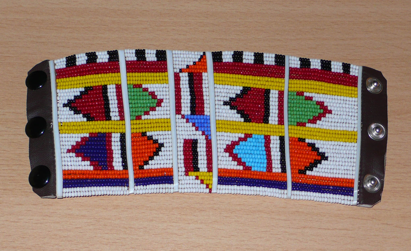 Bracelet africain pour enfant à motifs ethniques traditionnels Massai composé de trente-six rangées de perles de rocaille blanches et multicolores glissées sur des fils de fer fixés sur des charnières en plastique blanc.