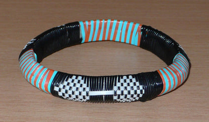 Bracelet africain à motifs tribaux, fabriqué au Mali dans une démarche eco-responsable, il est tressé à partir de fines bandes de plastique recyclé noir, blanc, orange et vert.