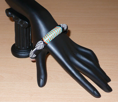 Bracelet africain à motifs tribaux, fabriqué au Mali dans une démarche eco-responsable, il est tressé à partir de fines bandes de plastique recyclé noir, blanc, orange et vert.